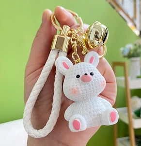 Detail of white resin bunny keychain with woven leather strap and golden bells