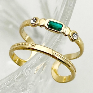 Gold open rings set with emerald green stone and textured band on glass display