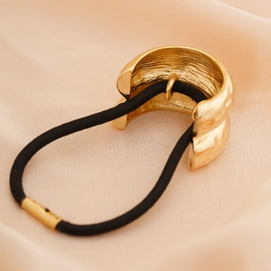 Close-up of golden hammered metal ponytail cuff with black elastic on champagne silk