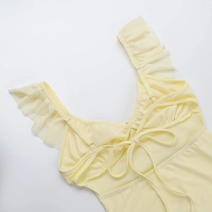 Detail showing the ruffled shoulder straps and lace-up back design on the cream dress