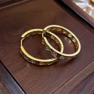 Detailed shot of golden hoop earrings with colorful zircon heart pattern on wooden background