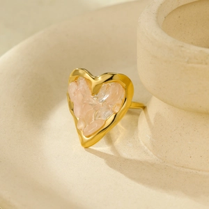 Detail of 18K gold heart ring featuring natural pink stone inlay on textured ceramic tray