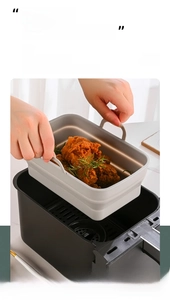Lifting a grey silicone liner with handles out of an air fryer containing fried chicken
