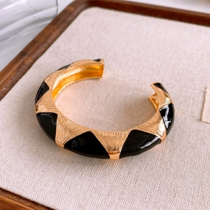 Detail view of gold cuff bangle with black enamel triangles and vertical brushed texture