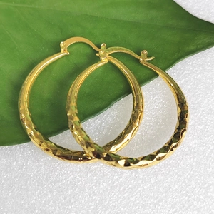 Textured gold hoop earrings with hammered metal finish displayed on a green leaf