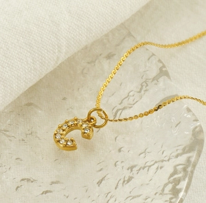 Macro shot of gold-plated letter C pendant with diamonds on a textured glass surface