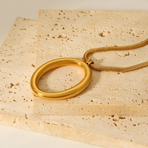 Detail of gold oval pendant necklace on a beige stone surface with snake chain style