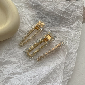 Detailed view of three resin hair clips with gold and silver sequins on white paper