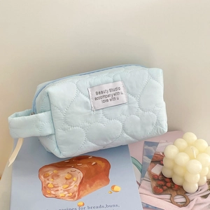 Close-up of light blue quilted heart makeup bag with side handle and zipper closure