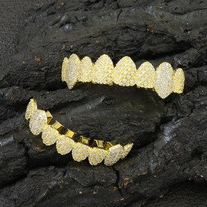 Iced out gold hip hop teeth grillz set with zircon stones on a black textured rock