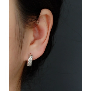 Macro detail of model wearing twisted silver hoop earrings with a polished textured finish