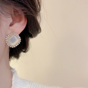 Macro shot of square opal earring with rhinestone border on female model's ear