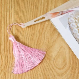 Détail d'un marque-page à pompon rose avec charme en résine et fleurs sur fond en bois