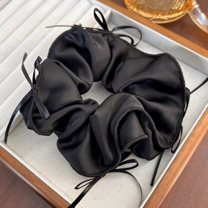 Detailed view of a black satin scrunchie featuring elegant small ribbon bows for hair