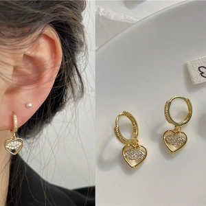 Detail of gold heart earrings with zircon evil eye design showing on-ear styling and product view