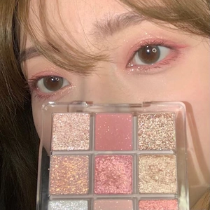 Close-up of a 9-color eyeshadow palette with matte and glitter pink shades held by a model