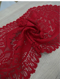 Close-up of red lace table runner with hollow floral pattern on light wooden surface