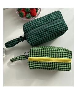 Detail of green houndstooth fabric pouches with metal ring zippers and wrist straps