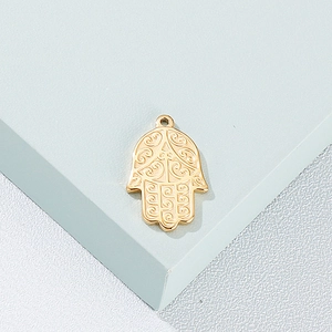 Macro view of a gold-plated Hamsa hand pendant with embossed patterns on a blue stand