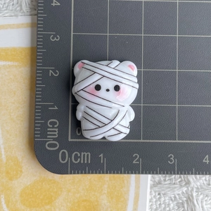 Macro shot of a cartoon mummy resin charm showing 2.5cm size scale on a grid mat