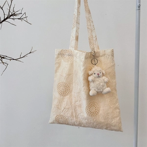 Close-up of intricate floral lace embroidery on a beige canvas tote bag with a plush lamb charm