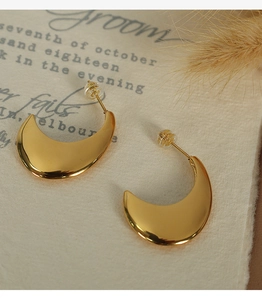 Detailed view of polished gold crescent earrings on a vintage paper with dried flowers