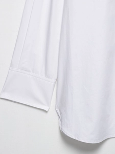 Close-up of white long sleeve blouse showing woven cotton texture and curved hemline