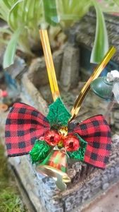 Close-up of golden Christmas bell with red and black plaid bow and holly berries