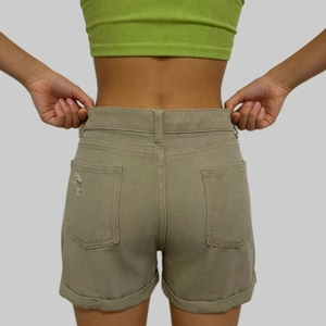 Dettaglio degli shorts in denim kaki che mostra la vita alta e gli orli sfilacciati