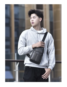 Men's black litchi grain leather sling bag worn across the body in a modern urban setting