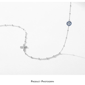 Detail of silver S925 cross pendant and evil eye bead necklace with fine chain