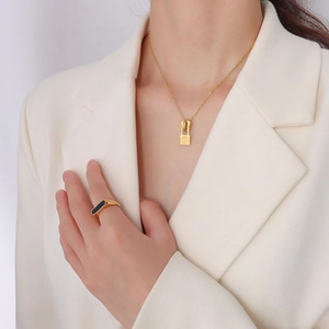 Detail of 18k gold plated necklace with lock pendant and black enamel ring on model