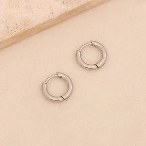 Minimalist silver titanium steel hoop earrings on a textured beige background