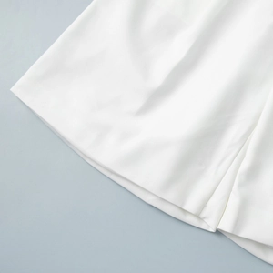 Detailed close-up of white woven shorts hem showing premium stitching and fabric texture