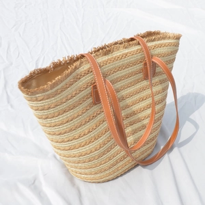 Handcrafted straw tote bag with brown leather handles and fringe trim for vacation