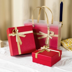 Three red gift boxes of various sizes with golden bows and a translucent carrier bag