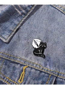 Détail d'un pin's en émail chat noir de dessin animé sur une veste en jean bleu