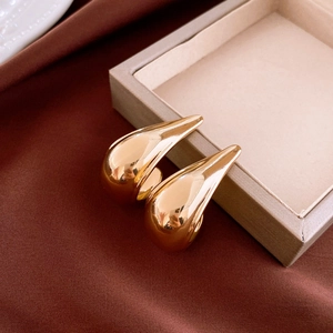 Polished gold curved drop earrings displayed on a beige jewelry box with red silk