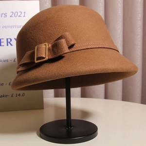 Chapeau cloche vintage en laine camel avec nœud et boucle métallique sur support noir