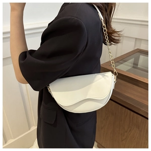 Détail d'un sacoche blanche avec une bandoulière chaîne dorée porté par un mannequin