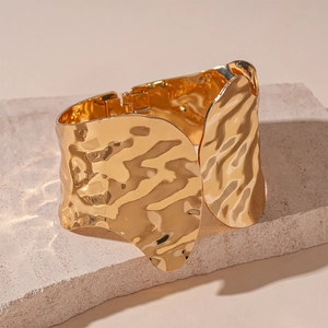 Detailed macro view of wide golden hammered metal cuff bracelet with unique rippled texture
