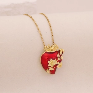 Golden necklace with red heart pendant featuring floral patterns on beige fabric
