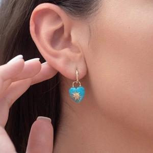 Detail shot of heart-shaped turquoise earring with starburst motif on a gold hoop