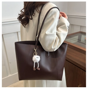 Detail view of a large brown leather tote bag with a plush charm on a female model