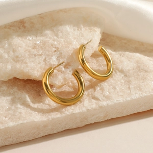 Minimalist thick gold C-shaped hoop earrings on white stone and satin background