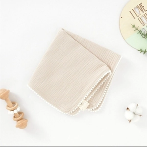 Détail d'une serviette en gaze de coton pour bébé avec bordure à pompons et décor