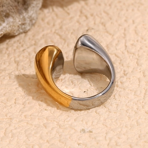 Bague ouverte bicolore or et argent en forme de goutte sur un fond de pierre beige