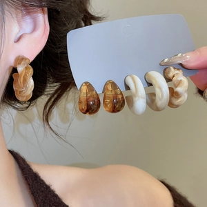 Detailed view of acrylic C-shaped earring set in amber and cream finishes on a display card