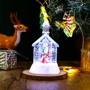 Close-up of a lit Christmas church snow globe with Santa Claus on a rustic wooden base