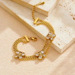 Double-layered gold-plated butterfly bracelet with clear crystals on beige stone background